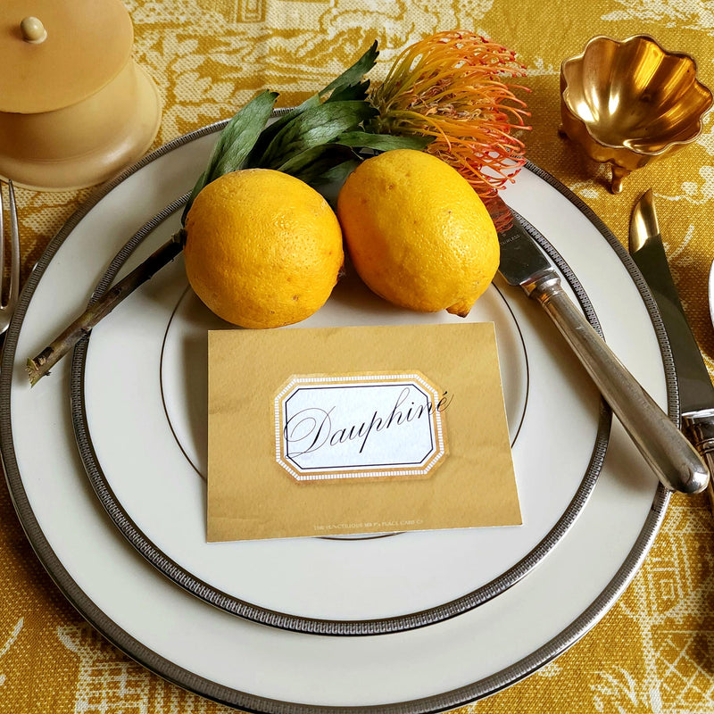 The Punctilious Mr. P's place card co. 'Envoy- Soleil' shades of yellows laydown event size custom place cards on printed tablecloth tablescape with fresh flowers and vintage silver cutlery