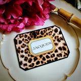 A leopard-print place card lettered with a guest's name in serif capitals, on a gold-rimmed plate