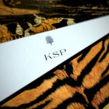 A note card personalized with a three-letter monogram beneath the anthemion motif, over tiger print