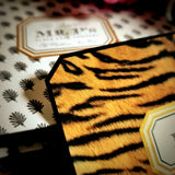Close-up of a tiger-print place card's clipped corner resting on the anthemion-print folio