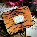 A tiger-print note card with a three-letter monogram in script, on a chinoiserie lacquer table beside a hand-lettered envelope