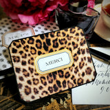 A leopard-print "MERCI" note card on a chinoiserie tray with a Mr. P's gift box, peonies and a hand-addressed envelope