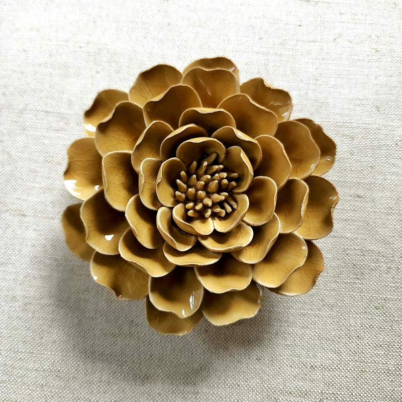 Ceramic flower resembling an caramel colored Peony, displayed on a dinner table with green foliage and elegant tableware.