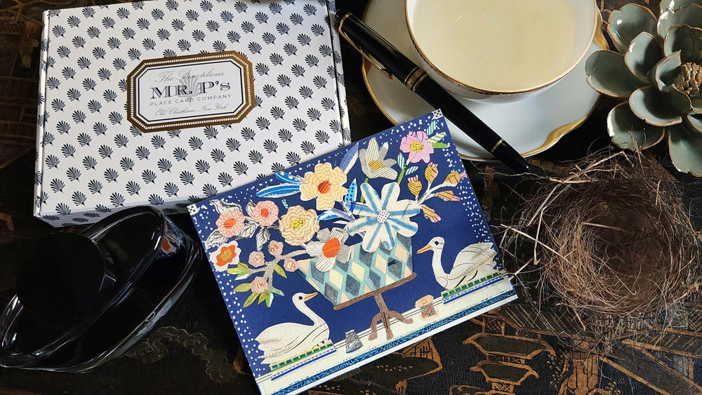 The Punctilious Mr. P's Place Card Co. X Sarah V Battle collaboration featuring "the swan" from "The Doves and Swans" fine note card set on a chinoiserie table with a cup of tea, montblanc fountain pen and our signature black and white anthemion pattern box