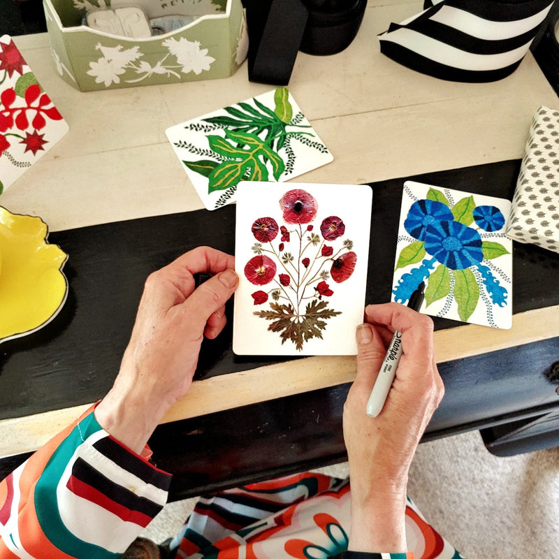 Marian Mcevoy hold a pressed poppy botanical custom note card in her hands at her black and white stripe writing desk