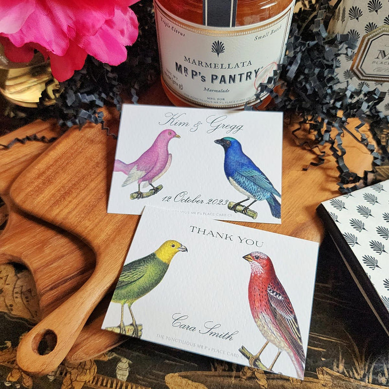showing both designs of The Punctilious Mr. P's Place Card Co. "Chromatic Cuckoo" Custom Gift Notes on a chinoiserie table with marmalade jam, cutting board and fresh flowers