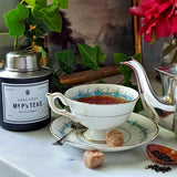 The Punctilious Mr. P's Earl Grey black Tea canister with tea cup and saucer, loose tea in a saucer on a marble table and a vintage silver plated teapot in the background