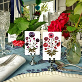 Marian McEvoy x The Punctilious Mr. P's Place Card Co collab with red and purple pressed poppies botanical illustrated custom place cards on a table with silverware, beautiful roses and fine cut crystal