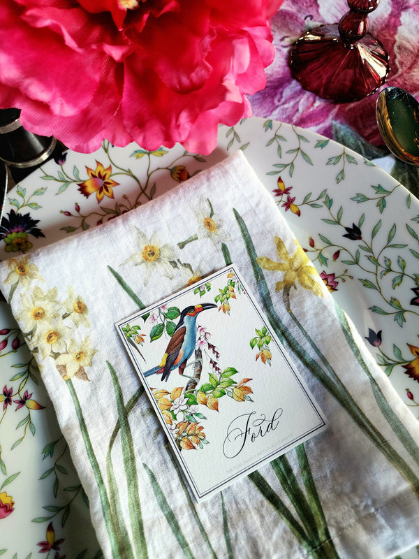 place card placed on a floral-patterned surface with pink flowers and a glass bottle.