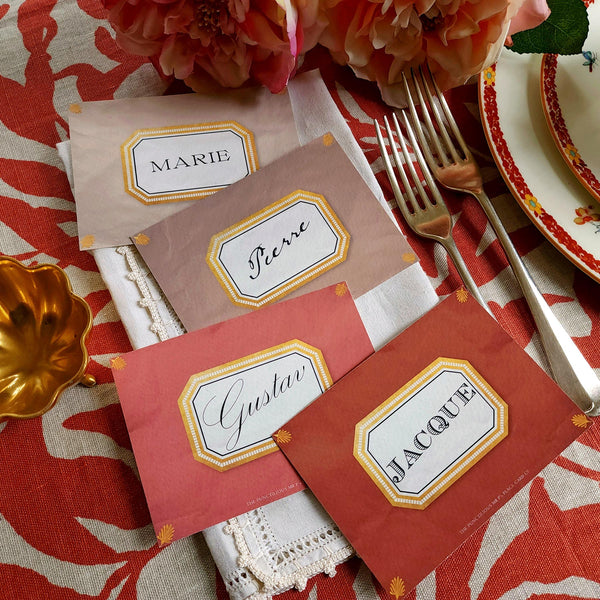 showing all 4 hues of The Punctilious Mr. P's place card co. 'Envoy- Brique' shades of reds laydown Event size custom place cards on printed tablecloth tablescape with fresh flowers and vintage silver cutlery