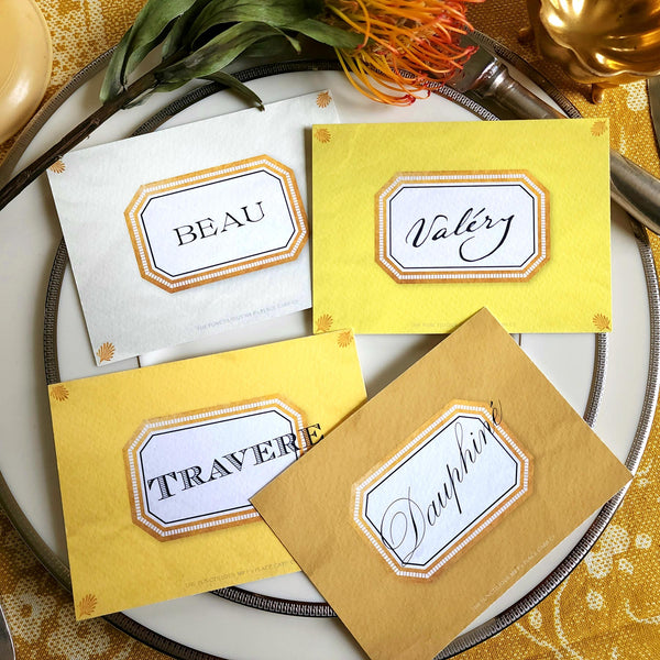 showing all 4 of The Punctilious Mr. P's place card co. 'Envoy- Soleil' shades of yellows laydown event size custom place cards on printed tablecloth tablescape with fresh flowers and vintage silver cutlery