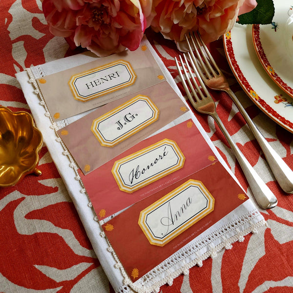 showing all 4 hues of The Punctilious Mr. P's place card co. 'Envoy- Brique' shaded of reds laydown size custom place cards on printed tablecloth tablescape with fresh flowers and vintage silver cutlery