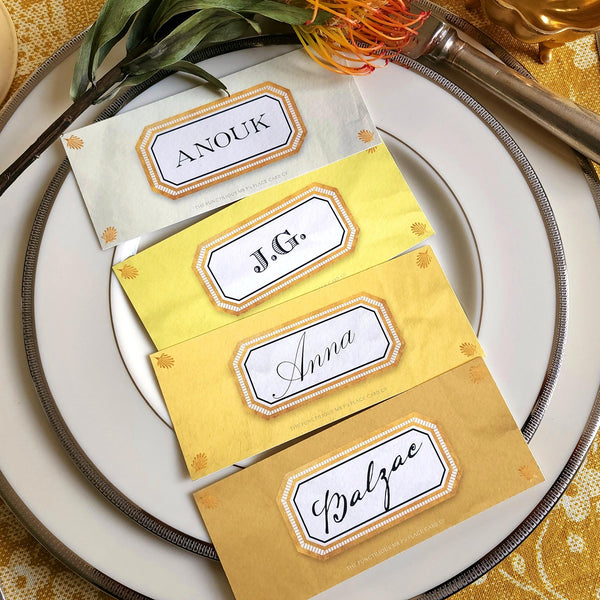 showing all 4 hues of The Punctilious Mr. P's place card co. 'Envoy- Soleil' shades of yellows laydown size custom place cards on printed tablecloth tablescape with fresh flowers and vintage silver cutlery