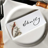 The Punctilious Mr. P's Place Card Co. 'Fanciful Pheasants' custom laydown place card on top of a white dinner plate and bamboo cutlery
