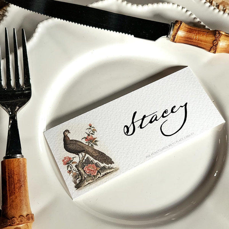 The Punctilious Mr. P's Place Card Co. 'Fanciful Pheasants' custom laydown place card on top of a white dinner plate and bamboo cutlery