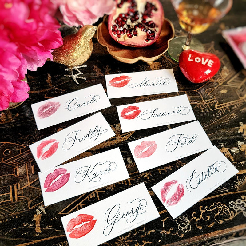 showing all 8 of The Punctilious Mr. P's Place Card Co. 'kisses' custom laydown size place cards on black and gold china tablescape with fresh flowers, pomegranate and bamboo cutlery