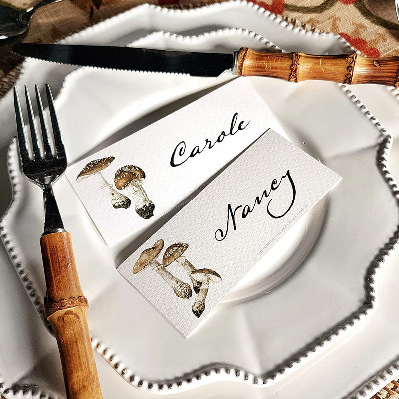 showing both designs of The Punctilious Mr. P's "Pantherina Mushrooms" laydown illustrated place cards on a white dinner plate with bamboo cutlery
