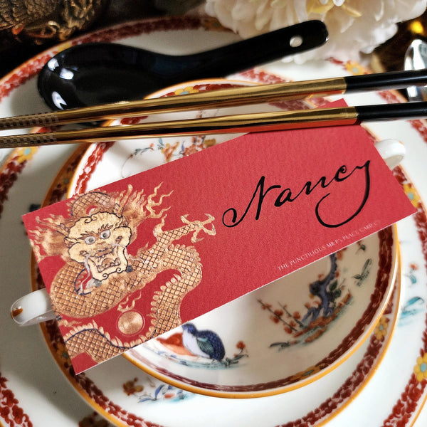 The Punctilious Mr. P's Place Card Co. "Radiant Dragon-Cinnabar" illustrated laydown place card featuring a golden-hue dragon on a chinoiserie set of china with golden chop sticks