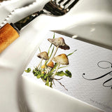 The Punctilious Mr. P's "Pantherina Mushrooms" laydown illustrated place cards on a white dinner plate with bamboo cutlery