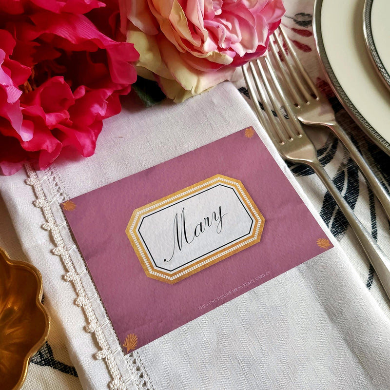 The Punctilious Mr. P's place card co. 'Envoy- Aubergine' shaded of purples laydown size custom place cards on printed tablecloth tablescape with fresh flowers and vintage silver cutlery showing the Spencerian script font