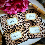 Four leopard-print place cards fanned across a gold-rimmed plate, each name in a gold-framed cartouche