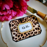 A leopard-print place card with clipped corners and a two-letter monogram in a gold-framed cartouche, on a gold-rimmed plate with a pink peony, from the Punctilious Mr. P's Place Card Company