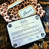 A clipped-corner card printed "MÉTIER PROVENANCE CARD" with the leopard design's story, signed in blue ink by both cofounders, over leopard-print place cards calligraphed with a guest's name in script, on a chinoiserie lacquer table