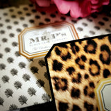 Close-up of a leopard-print note card's clipped corner resting on the anthemion-print folio