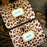 Two leopard-print note cards on a chinoiserie lacquer table, monograms in script and in serif capitals