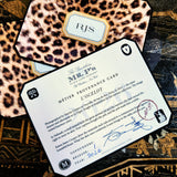 A clipped-corner card printed "MÉTIER PROVENANCE CARD" with the leopard design's story, signed in blue ink by both cofounders, over a leopard-print note card with a two- to three-letter monogram in serif capitals, on a chinoiserie lacquer table