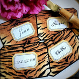 Four tiger-print place cards fanned across a gold-rimmed plate, each name in a gold-framed cartouche