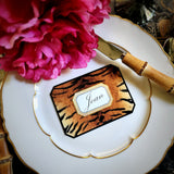 A tiger-print place card lettered with a guest's name in script, on a gold-rimmed plate beside a peony