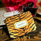 A tiger-print note card reading "MERCI" in serif capitals, propped against a crystal ink bottle on a chinoiserie lacquer table