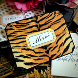 A tiger-print note card reading "Merci" in script, beside a hand-addressed envelope