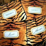 Four tiger-print thank you note cards reading "Merci", two in script and two in serif capitals