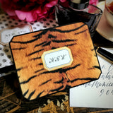 A tiger-print note card with a three-letter monogram in script within a gold-framed cartouche, beside an ink bottle and a hand-lettered envelope, from the Punctilious Mr. P's Place Card Company