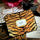 A tiger-print note card with a three-letter monogram in serif capitals within a gold-framed cartouche