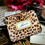 A leopard-print note card reading "Merci" in script, styled with a fountain pen, ink bottle and gift box