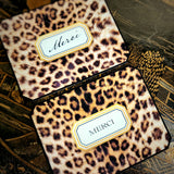 Two leopard-print thank you note cards, one reading "Merci" in script and one in serif capitals, on a chinoiserie lacquer table