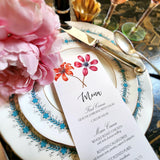 The Punctilious Mr. P's Place Card Co. "Anemones" menu card on a blue and white dinner plate with a bright pink peony next to it