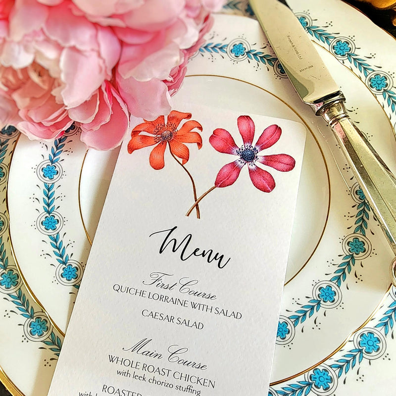 The Punctilious Mr. P's Place Card Co. "Anemones" menu card on a blue and white dinner plate with a bright pink peony next to it