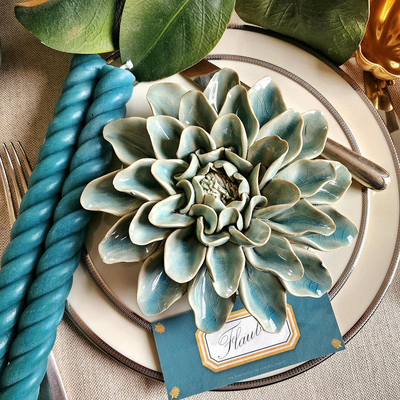 Ceramic flower resembling a celadon Dinner Plate Dahlia, displayed on a dinner table with green foliage and elegant tableware with marine colored Envoy laydown place card and matching rope candles