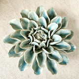 Ceramic flower resembling a celadon Dinner Plate Dahlia, displayed on a dinner table with green foliage and elegant tableware with marine colored Envoy laydown place card