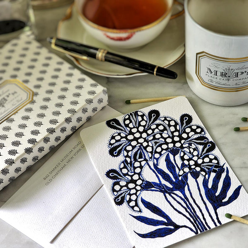 Marian McEvoy x The Punctilious Mr. P's Place Card Co collab with blue botanical illustrated custom note cards called 'Floral Fantasia' on a table with a montblanc fountain pen, tea cup and saucer and Mr. P's candle