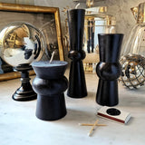 3 black pillar candles on white marble table with a stainless steel orb and base and a small box of matches