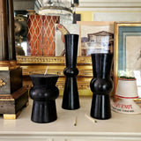 3 black pillar candles on a mantle with chandelier in the background