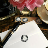 The Punctilious Mr. P x Sarah V Battle fine note card set featuring the packaging of the envelopes with sun face sealing wafer, on chinoiserie table with Mr. P's I conic black and white anthemion print. montblanc fountain pen resting on top