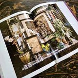 Open book showing a decorative interior scene with plants and decor.