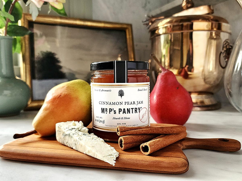 mr. p's pantry cinnamon pear jam on a chic teak cutting board with a pear, cinnamon sticks and a block of cheese.