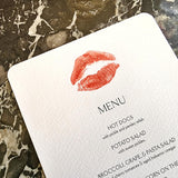 The Punctilious Mr. P's Place Card Co. 'Kisses' custom Mayfair size menu of lips on a black marble tabletop